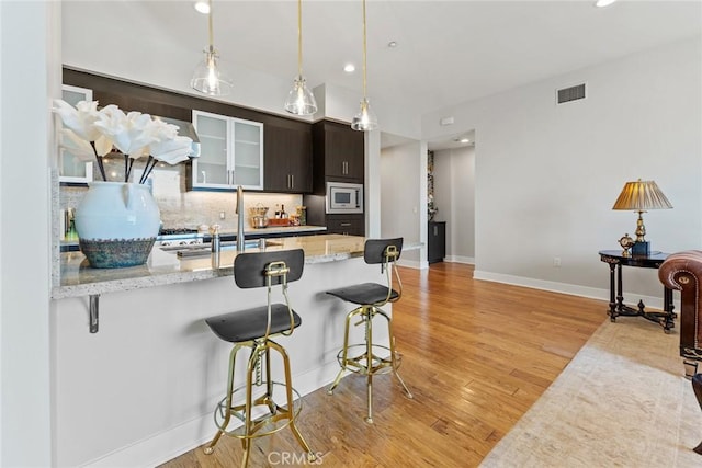 402 Rockefeller Unit 407, Irvine, CA 92612 - kitchen featuring a breakfast bar, stainless steel microwave, a sink, light wood-style flooring, and decorative backsplash