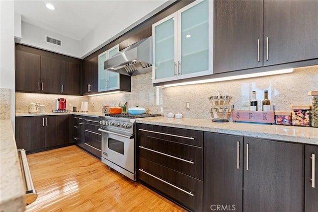 402 Rockefeller Unit 407, Irvine, CA 92612 - kitchen with high end stainless steel range oven, wall chimney range hood, dark brown cabinetry, light wood-style floors, and light stone countertops