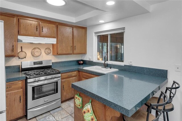 9945 Date St, Fontana, CA 92335 - kitchen with under cabinet range hood, stainless steel gas range oven, a sink, a peninsula, and dark countertops
