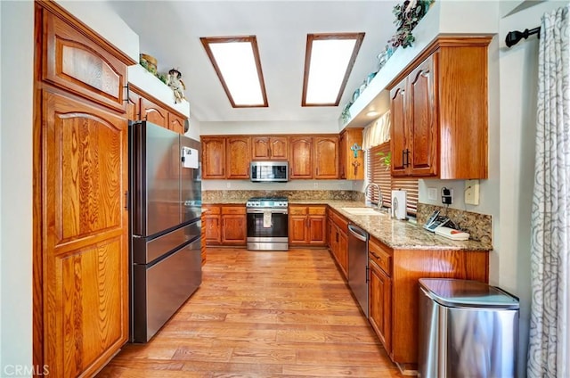 42635 56th St W, Lancaster, CA 93536 - kitchen featuring stainless steel appliances, brown cabinetry, a sink, light wood-style floors, and light stone counters