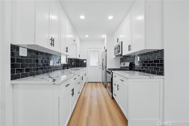 611 S Thorson Ave, Compton, CA 90221 - kitchen with stainless steel appliances, a sink, light wood-type flooring, backsplash, and white cabinets