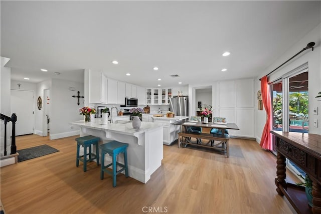 1528 Hendrix Pl, Chula Vista, CA 91911 - kitchen with stainless steel appliances, a peninsula, light wood finished floors, white cabinets, and glass insert cabinets