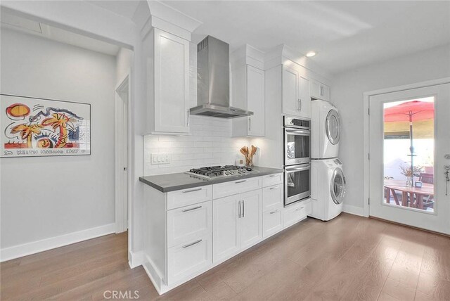 256 Falcon Ave, Long Beach, CA 90802 - kitchen featuring wall chimney range hood, appliances with stainless steel finishes, stacked washer / dryer, wood finished floors, and white cabinets