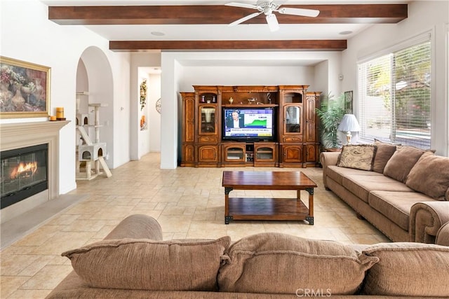 11538 Stoney Brook Ct, Beaumont, CA 92223 - living room with beam ceiling, a ceiling fan, stone tile floors, a glass covered fireplace, and arched walkways