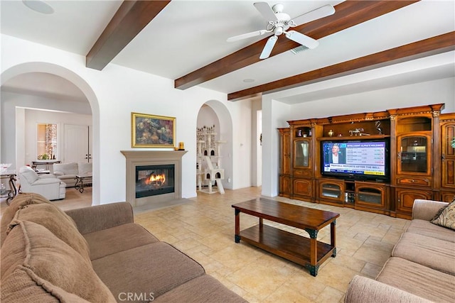 11538 Stoney Brook Ct, Beaumont, CA 92223 - living room featuring stone tile flooring, arched walkways, beamed ceiling, ceiling fan, and a fireplace with flush hearth