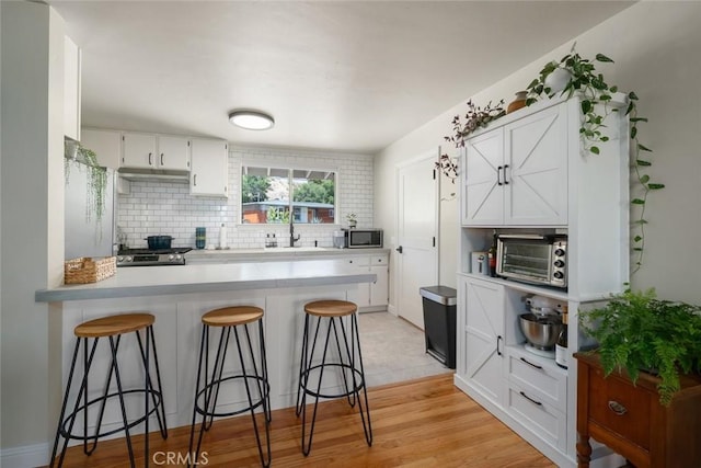 1215 Sylvia Ct, San Luis Obispo, CA 93401 - kitchen featuring stainless steel microwave, a peninsula, a breakfast bar, white cabinets, and tasteful backsplash