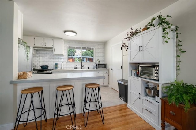 1215 Sylvia Ct, San Luis Obispo, CA 93401 - kitchen featuring stainless steel appliances, a peninsula, a breakfast bar, white cabinetry, and decorative backsplash