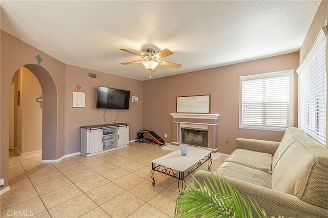 5531 Cordiva Ct, Lancaster, CA 93536 - living area featuring arched walkways, ceiling fan, a glass covered fireplace, light tile patterned flooring, and a textured ceiling