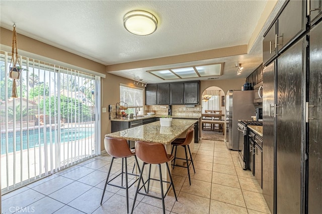 5531 Cordiva Ct, Lancaster, CA 93536 - kitchen featuring appliances with stainless steel finishes, a kitchen breakfast bar, a center island, a textured ceiling, and light tile patterned flooring