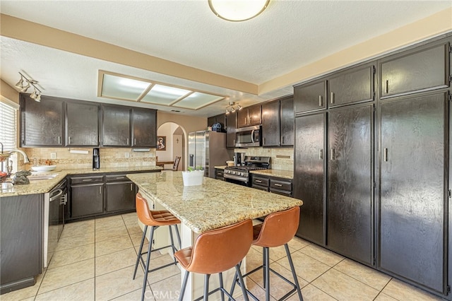 5531 Cordiva Ct, Lancaster, CA 93536 - kitchen with stainless steel appliances, a sink, arched walkways, decorative backsplash, and a textured ceiling