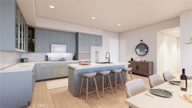 581 Higuera St Unit 208, San Luis Obispo, CA 93401 - kitchen with a sink, a breakfast bar, decorative backsplash, a center island with sink, and light wood-style floors