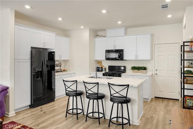 1095 W Buttercup Ln, Rialto, CA 92376 - kitchen with black appliances, light wood-style flooring, a kitchen island with sink, a kitchen bar, and white cabinetry