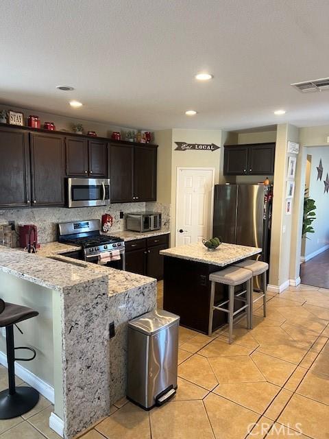 3762 Segovia Dr, Perris, CA 92571 - kitchen with stainless steel appliances, a breakfast bar area, light stone countertops, tasteful backsplash, and light tile patterned floors