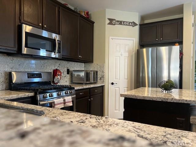 3762 Segovia Dr, Perris, CA 92571 - kitchen featuring appliances with stainless steel finishes, dark brown cabinetry, backsplash, and light stone counters