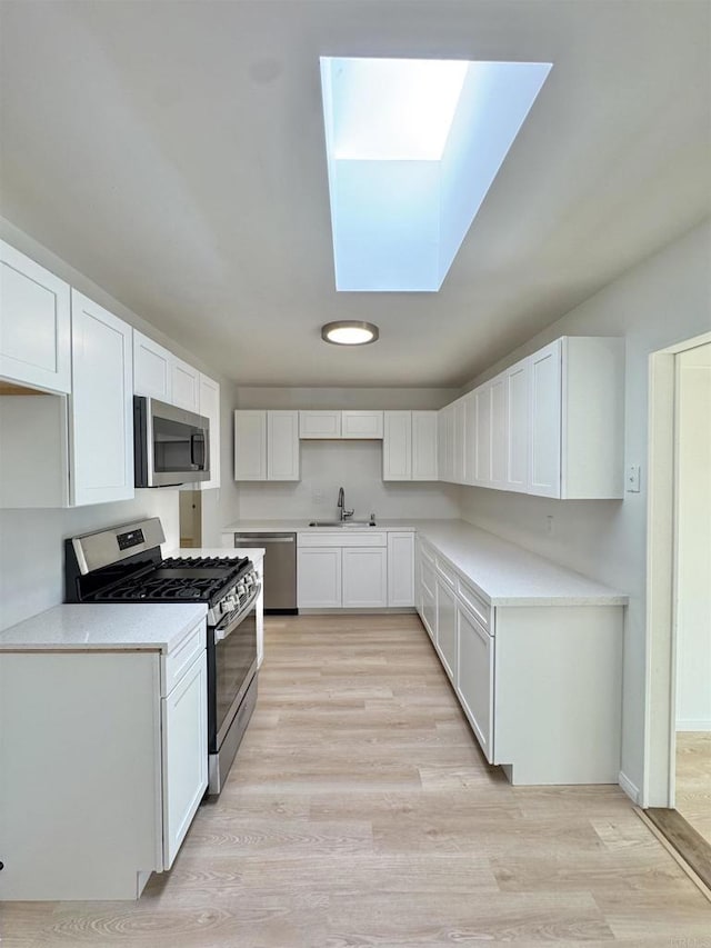 1335 S Hickory St, Anaheim, CA 92805 - kitchen with stainless steel appliances, a skylight, a sink, light wood finished floors, and white cabinetry