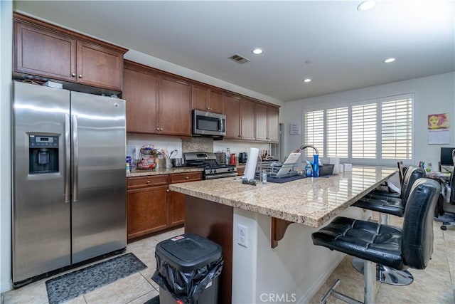 15345 Chive Ln, Fontana, CA 92336 - kitchen with stainless steel appliances, a kitchen breakfast bar, recessed lighting, light stone countertops, and a kitchen island with sink