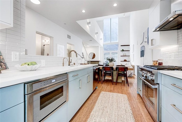 1436 N Detroit St Unit 2, Los Angeles, CA 90046 - kitchen with wall chimney range hood, appliances with stainless steel finishes, backsplash, light wood-type flooring, and recessed lighting