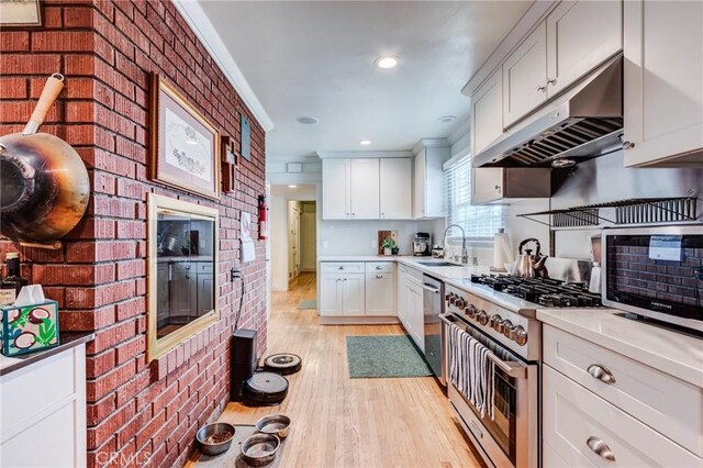 12438 Lambert Cir, Garden Grove, CA 92841 - kitchen with appliances with stainless steel finishes, under cabinet range hood, brick wall, light wood-type flooring, and a sink