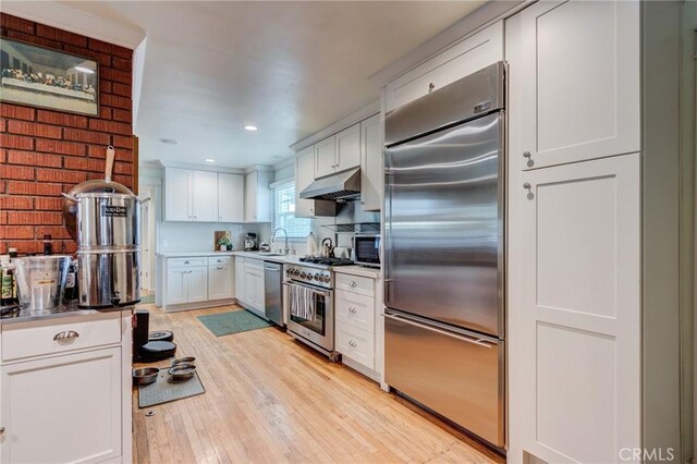 12438 Lambert Cir, Garden Grove, CA 92841 - kitchen with high quality appliances, light wood-style floors, white cabinetry, under cabinet range hood, and a sink