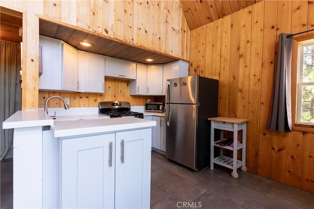 26503 Amador Ln, Lake Arrowhead, CA 92352 - kitchen with stainless steel appliances, wooden walls, a peninsula, vaulted ceiling, and white cabinetry