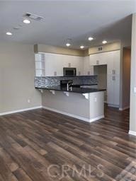159 E Commercial St, San Dimas, CA 91773 - kitchen with stainless steel microwave, dark countertops, baseboards, a peninsula, and dark wood-style floors