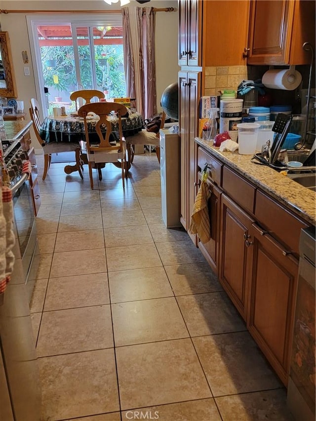 7571 San Rafael Dr E, Buena Park, CA 90620 - kitchen with brown cabinetry, stainless steel gas stove, light tile patterned floors, and tasteful backsplash
