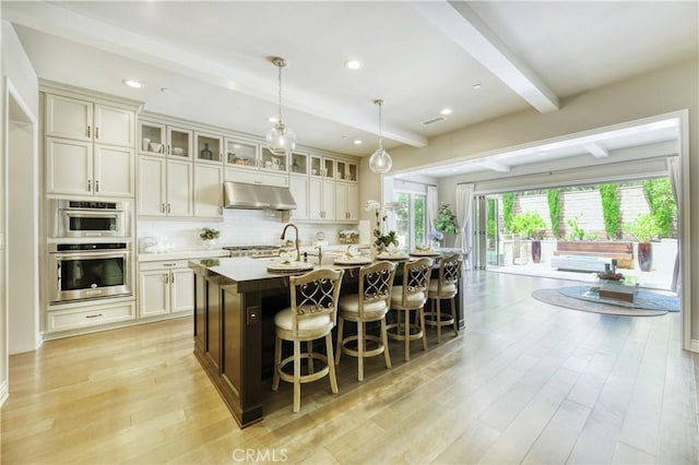 46 Shadybend, Irvine, CA 92602 - kitchen featuring beam ceiling, light wood-style floors, under cabinet range hood, a kitchen island with sink, and a kitchen breakfast bar