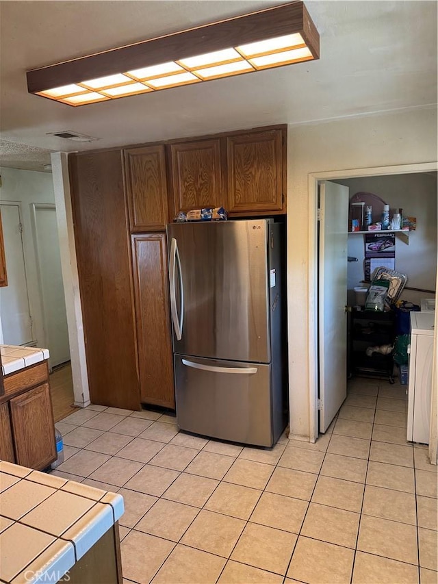 14222 Filmore St, Arleta, CA 91331 - kitchen featuring freestanding refrigerator, tile countertops, light tile patterned flooring, washer / clothes dryer, and brown cabinetry