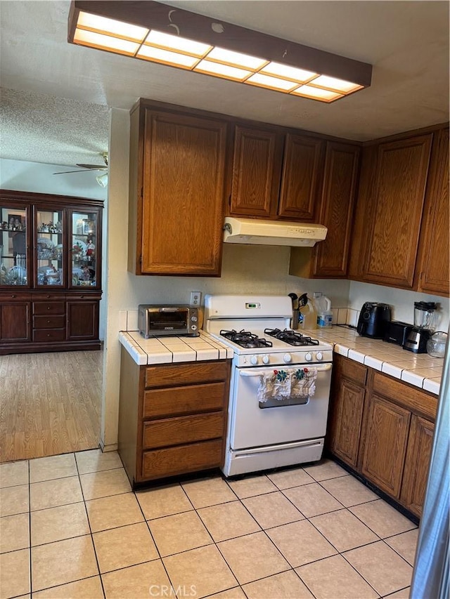 14222 Filmore St, Arleta, CA 91331 - kitchen featuring white range with gas cooktop, under cabinet range hood, tile counters, light tile patterned floors, and a ceiling fan