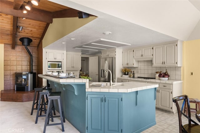 558 Paseo Companeros St, Chico, CA 95928 - kitchen featuring stainless steel appliances, tile counters, a wood stove, a sink, and a breakfast bar area
