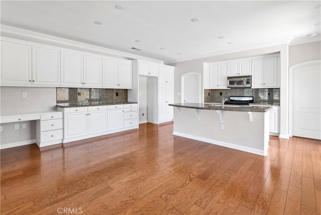 243 Firestone, Hemet, CA 92545 - kitchen with stainless steel microwave, decorative backsplash, arched walkways, range, and ornamental molding