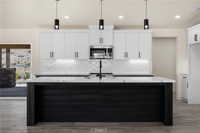 9641 Buena Vista St, Apple Valley, CA 92308 - kitchen with stainless steel microwave, an island with sink, white cabinets, tasteful backsplash, and hanging light fixtures