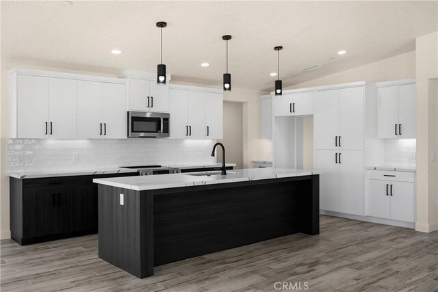 9641 Buena Vista St, Apple Valley, CA 92308 - kitchen with stainless steel microwave, a kitchen island with sink, decorative backsplash, light wood-style flooring, and white cabinetry