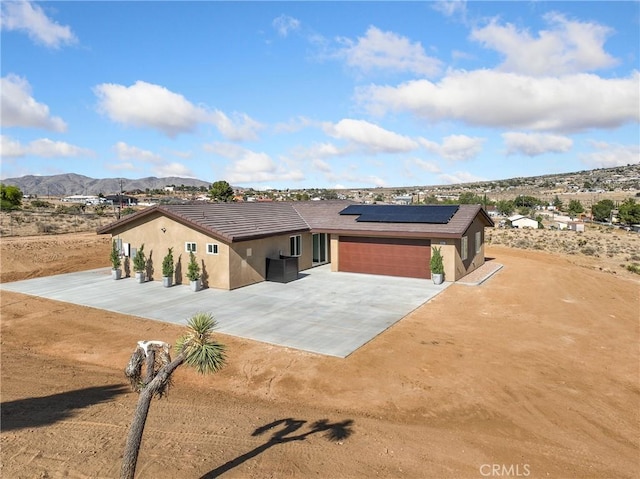 9641 Buena Vista St, Apple Valley, CA 92308 - view of front of house with stucco siding, a mountain view, driveway, and roof mounted solar panels