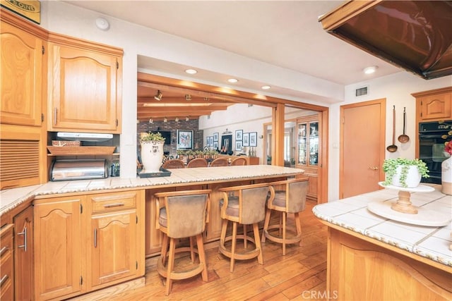 3152 Parkside Dr, San Bernardino, CA 92404 - kitchen featuring light wood-type flooring, a peninsula, tile counters, extractor fan, and recessed lighting