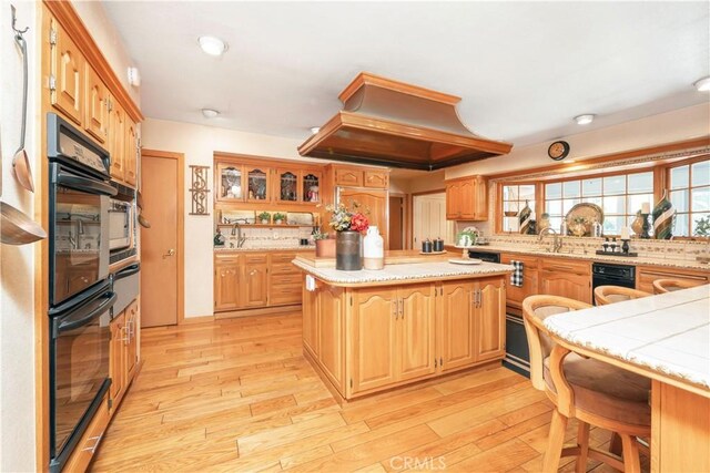 3152 Parkside Dr, San Bernardino, CA 92404 - kitchen with premium range hood, light countertops, a kitchen island, light wood-type flooring, and glass insert cabinets