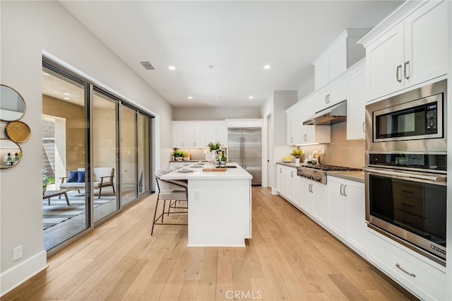 126 Paxton, Irvine, CA 92620 - kitchen with built in appliances, under cabinet range hood, white cabinetry, light wood-type flooring, and light countertops