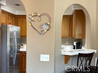 39244 Turtle Bay Ln Unit F, Murrieta, CA 92563 - kitchen with stainless steel fridge with ice dispenser, brown cabinetry, arched walkways, a kitchen bar, and light countertops
