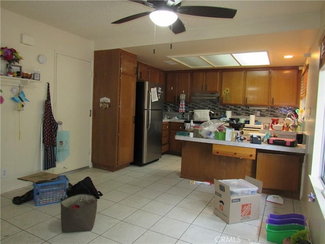 26250 Spaniel Ln, Menifee, CA 92586 - kitchen with freestanding refrigerator, a peninsula, brown cabinetry, backsplash, and ceiling fan