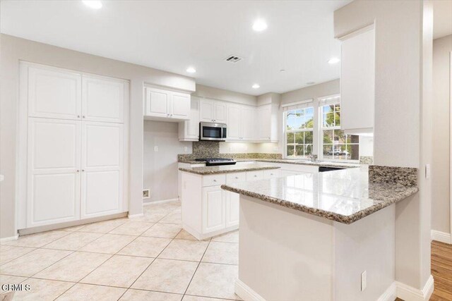 5611 Dorsey St, Ventura, CA 93003 - kitchen featuring stainless steel microwave, light stone counters, a peninsula, white cabinets, and backsplash
