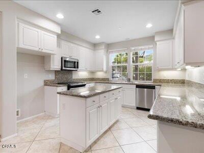 5611 Dorsey St, Ventura, CA 93003 - kitchen with appliances with stainless steel finishes, white cabinetry, light tile patterned floors, a kitchen island, and decorative backsplash