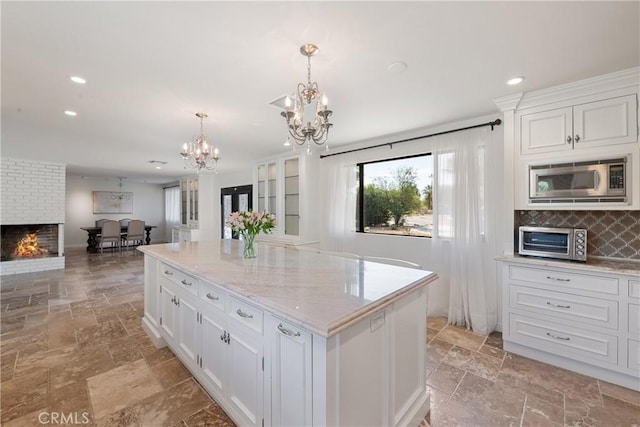 72408 Desert Dr, Rancho Mirage, CA 92270 - kitchen with a chandelier, stone tile floors, stainless steel microwave, white cabinets, and decorative backsplash