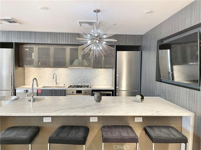 1050 S Grand Ave Unit 2003, Los Angeles, CA 90015 - kitchen featuring appliances with stainless steel finishes, a sink, a chandelier, light stone countertops, and a kitchen bar
