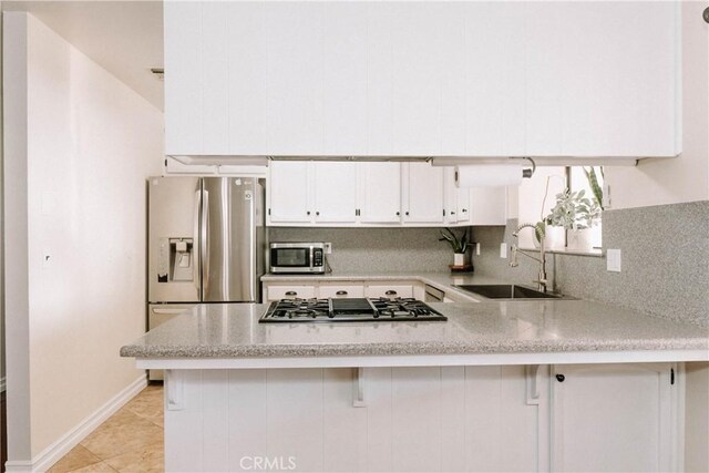 134 N American St, Ridgecrest, CA 93555 - kitchen featuring a sink, stainless steel appliances, a peninsula, white cabinetry, and backsplash