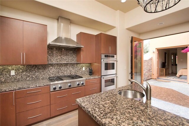 50135 Camino Privado Ln, Quinta, CA 92253 - kitchen with a sink, appliances with stainless steel finishes, wall chimney range hood, backsplash, and stone countertops