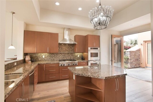 50135 Camino Privado Ln, Quinta, CA 92253 - kitchen with wall chimney exhaust hood, stainless steel appliances, brown cabinets, light wood-style flooring, and stone countertops
