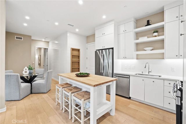 108 Coastal Gdn, Irvine, CA 92618 - kitchen featuring appliances with stainless steel finishes, a sink, open shelves, light wood-type flooring, and white cabinetry