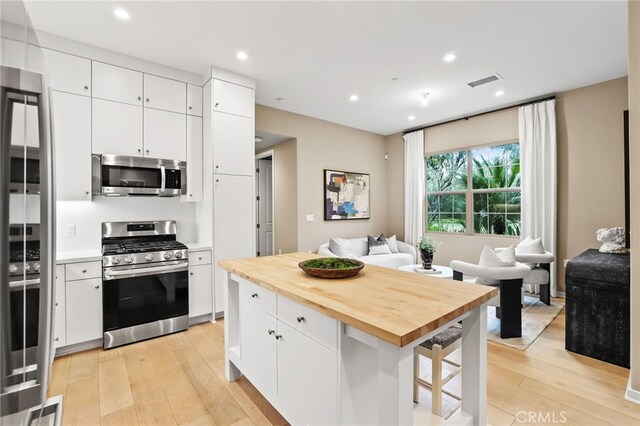 108 Coastal Gdn, Irvine, CA 92618 - kitchen featuring appliances with stainless steel finishes, light wood-style flooring, butcher block counters, open floor plan, and white cabinetry