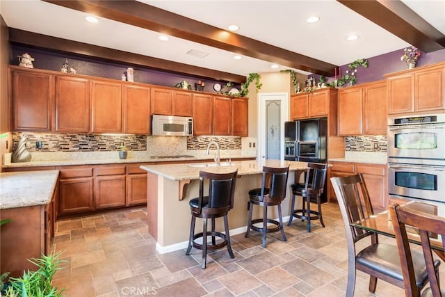 36235 Bay Hill Dr, Beaumont, CA 92223 - kitchen with stainless steel appliances, beam ceiling, backsplash, a center island with sink, and stone tile flooring