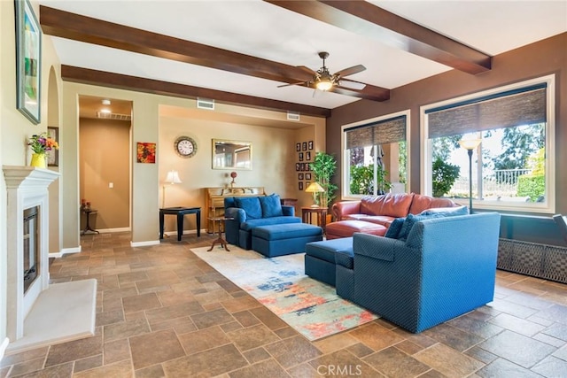 36235 Bay Hill Dr, Beaumont, CA 92223 - living room featuring stone tile flooring, beam ceiling, baseboards, a ceiling fan, and a glass covered fireplace